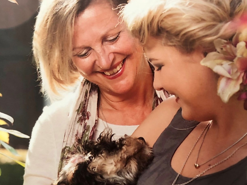 Two women laughing whilst looking down at a dog being held by one of the women